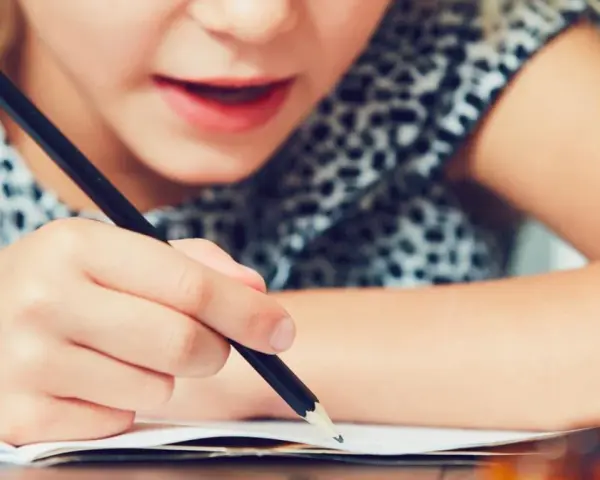 Dziecko zmagające się z pisaniem, co może być oznaką dysleksji. Skupienie na twarzy i ręce trzymającej ołówek.