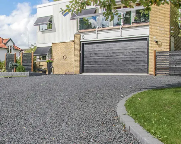 En vacker uppfart med mörkt grus leder fram till ett modernt hus med garageport.