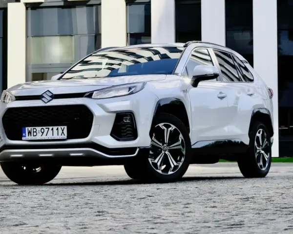Biały Suzuki Across z czarnymi detalami stoi przed nowoczesnym budynkiem.