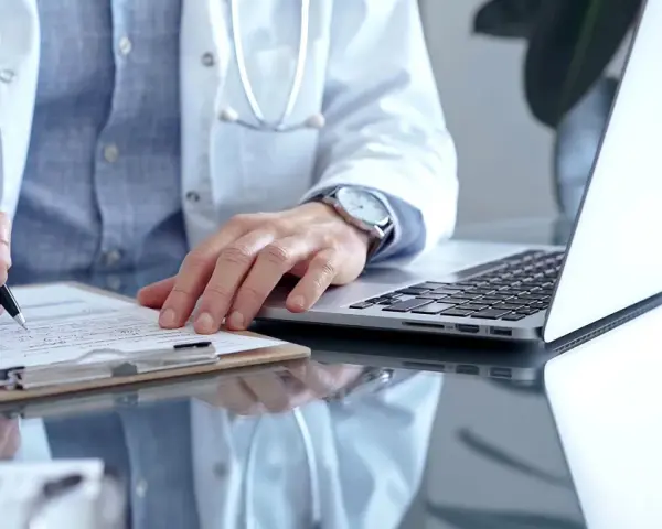 Lekarz w białym kitlu pisze na dokumentach, obok laptop. To może być zwolnienie od psychiatry.