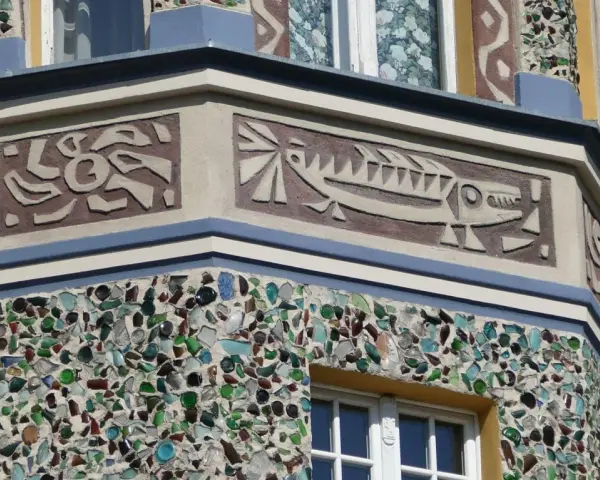 Sgraffito na fasadzie budynku: stylizowana ryba i abstrakcyjne wzory. Dolna część ozdobiona mozaiką z kolorowego szkła.