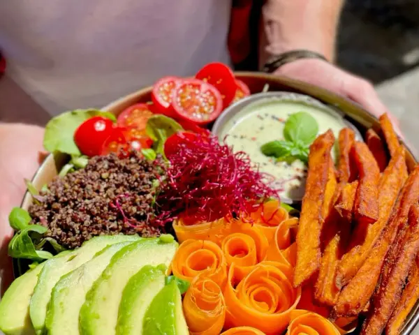 Ein bunter Buddha Bowl mit Avocado, Quinoa, Süßkartoffel-Pommes und Karottenrosen. Ein froindlichst Berlin-Genuss!