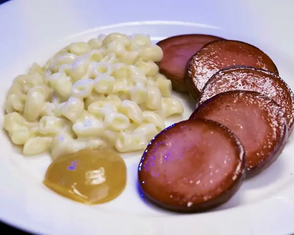 Stuvade makaroner snabbt vis med skivad falukorv och en klick senap på en vit tallrik.
