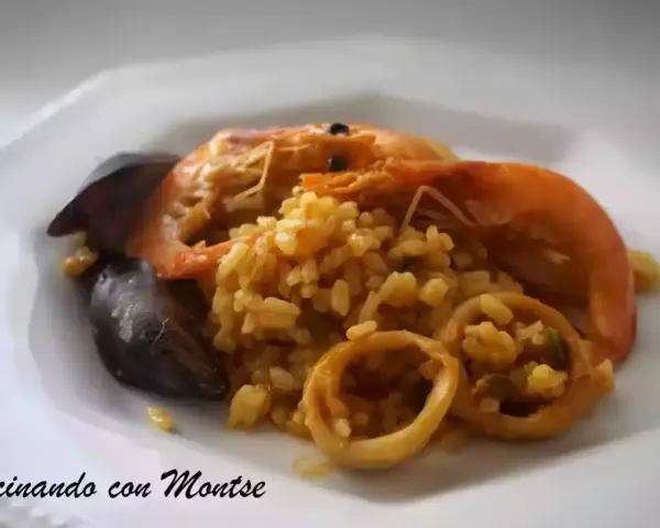 Arroz meloso con langostinos, mejillones y calamares en un plato blanco.