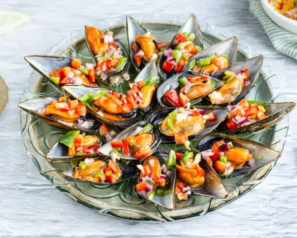 Mejillones a la vinagreta, frescos y coloridos, servidos en su concha con una picada de pimientos y cebolla.