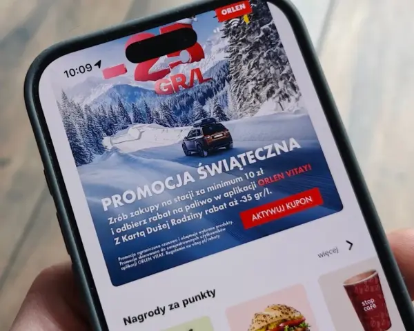 Aplikacja ORLEN z promocją na paliwo za punkty. Zima, góry i samochód na ekranie telefonu.