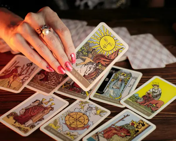 Dłoń z pierścionkiem wybiera kartę Słońce z talii tarot. Rozłożony krzyż celtycki tarot zapowiada przyszłość.