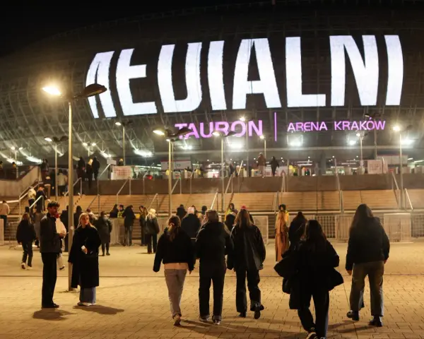 Tłum ludzi zmierza do Tauron Areny Kraków na koncert. Wielki napis na dachu obiektu zapowiada wydarzenie. To prawdziwy **rush w Polsce**!