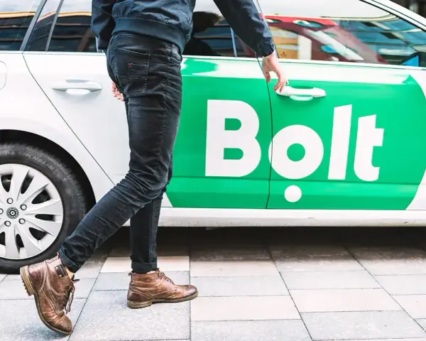 Chcesz wiedzieć, jak zostać kierowcą Bolta? Mężczyzna otwiera drzwi białego samochodu z zielonym logo Bolt.