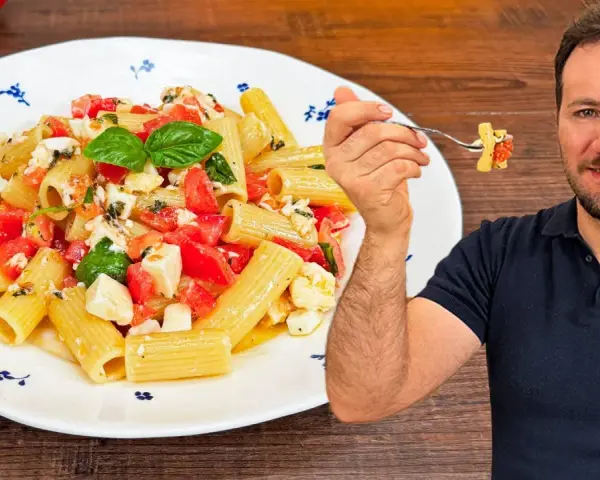 Un uomo sorride mentre assaggia una forchettata di pasta alla checca, un piatto fresco con pomodori, mozzarella e basilico.