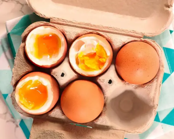 Uova alla coque in un cartone, alcune aperte mostrano tuorli dorati e cremosi, pronte per essere gustate.