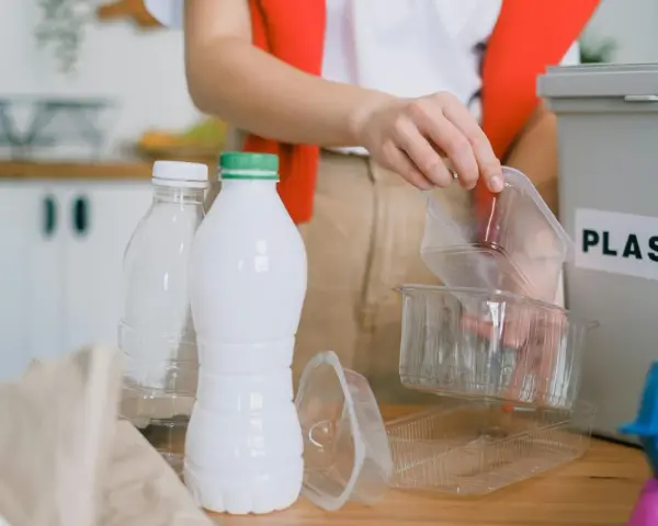 Segregacja odpadów to pierwszy krok, jak ograniczyć plastik. Ręka wrzuca plastikowe opakowania do pojemnika z napisem "PLASTIC".