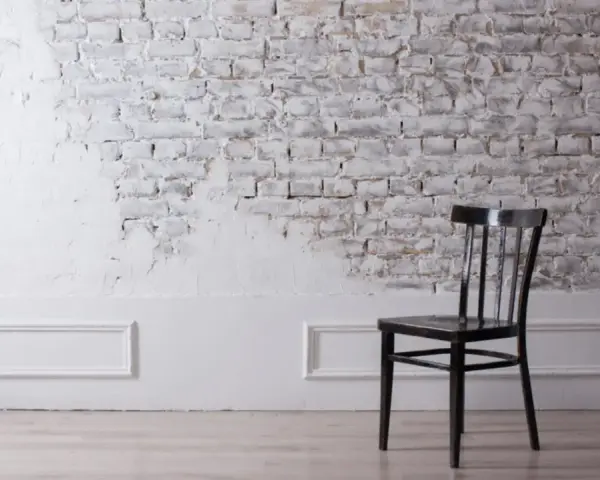 Silla negra frente a pared de ladrillo rústica, con un acabado de pintar pared de piedra en blanco que deja ver la textura original.
