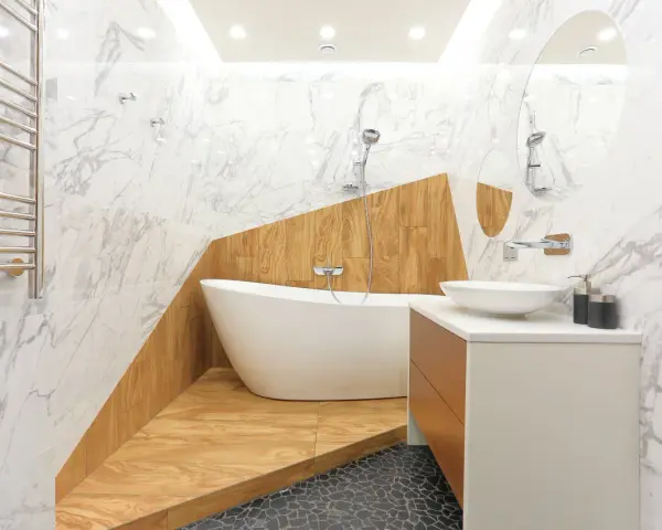 Salle de bain moderne avec baignoire îlot sur une estrade en bois, lavabo, miroir et carrelage marbre.