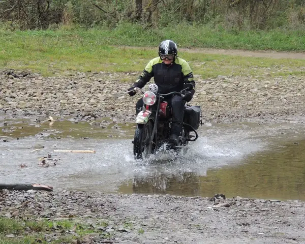 Motocyklista w kasku pokonuje wodną przeszkodę na kamienistej trasie w okolicach Jasła.