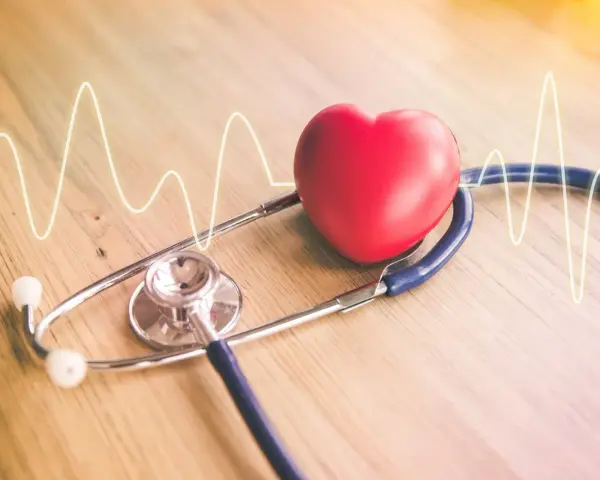 Czerwone serce i stetoskop na drewnianym tle z linią EKG.
