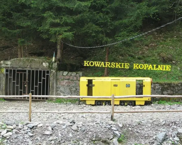 Wejście do sztolni Kowary z żółtym wagonikiem górniczym i napisem "KOWARSKIE KOPALNIE".