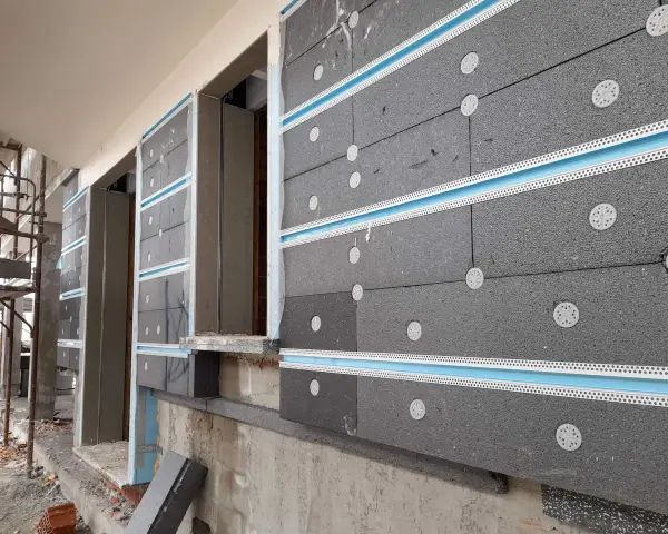 Pannelli grigi per cappotto termico ignifugo, fissati con tasselli bianchi e profili azzurri, in fase di installazione su un edificio.