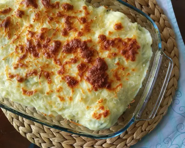Parmentier de patata gratinado en fuente de cristal, con queso dorado y burbujeante. Un plato reconfortante y delicioso.