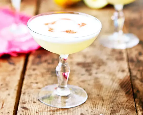 En krämig pisco sour med ett vitt skum och en touch av kanel på en rustik träyta.