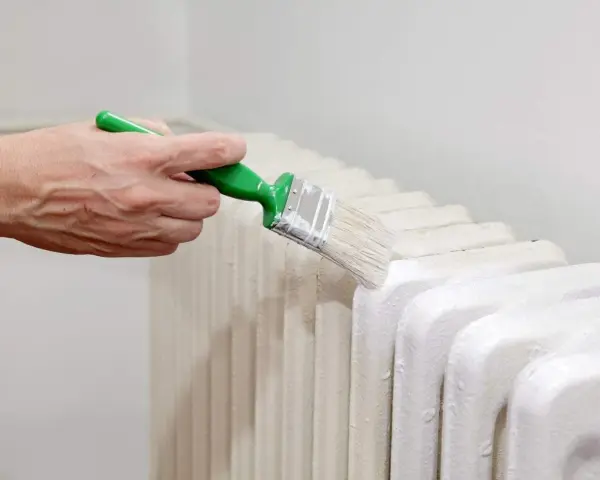 Main d'une personne peignant un radiateur en fonte avec une brosse.
