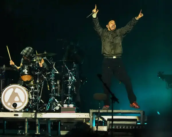 Linkin Park-Bandmitglieder auf der Bühne, ein Sänger springt, ein Schlagzeuger spielt.