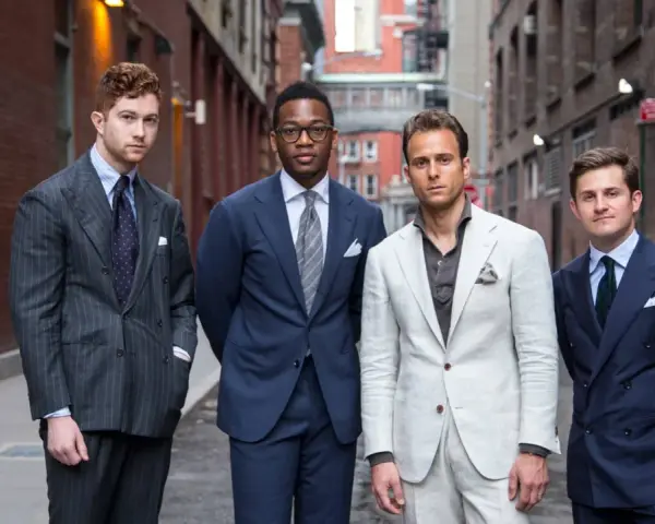 Quattro uomini in abiti eleganti, con un impeccabile bavero giacca, posano in un vicolo urbano.