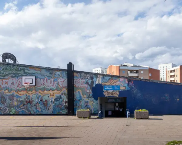 En stor vägg täckt av färgstark graffiti. En basketkorg hänger på väggen.