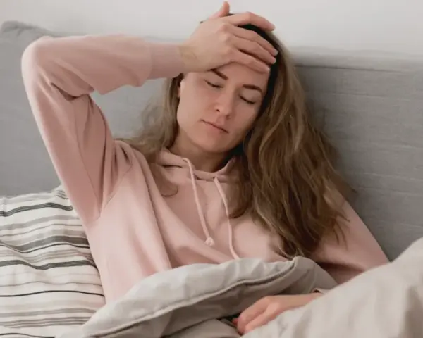 En kvinna med handen på pannan, insvept i täcken, upplever ångest direkt på morgonen.