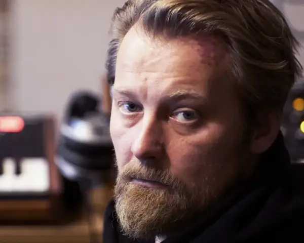 Bartek Dziedzic, z zarostem i lekko zaczerwienionym czołem, siedzi przed syntezatorami.