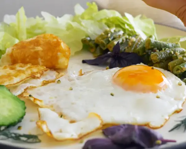 Un œuf au plat parfait, servi avec des haricots verts, des tranches de concombre, de la laitue et une touche de citron vert.