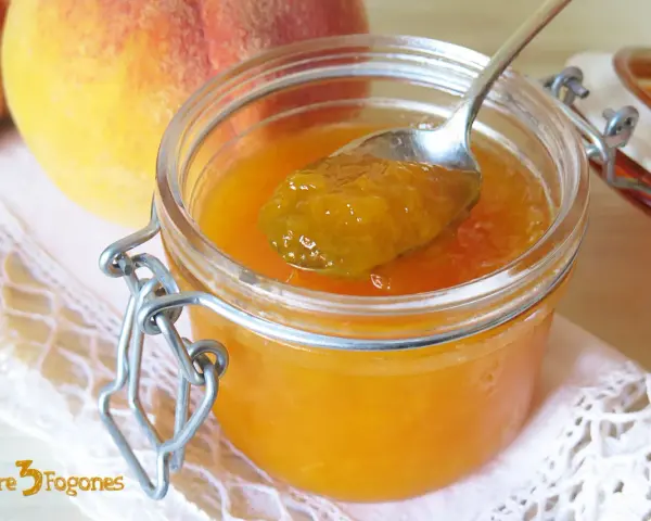 Cuchara con mermelada de melocotón casera, junto a melocotones frescos y un tarro de cristal.