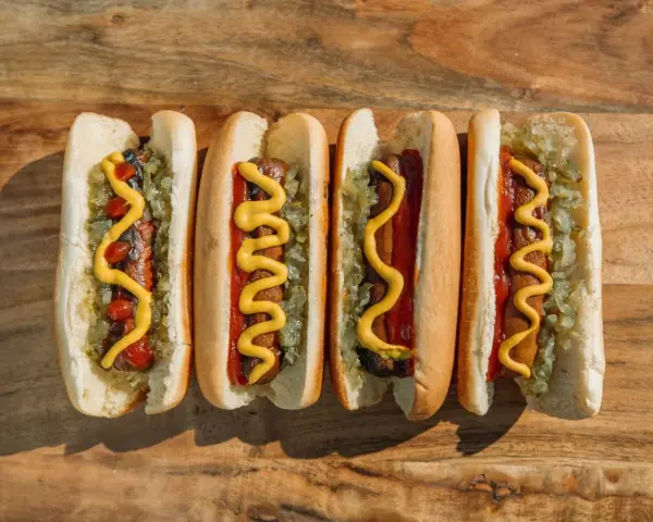 Cuatro hot dogs con mostaza, kétchup y cebolla picada sobre una tabla de madera.