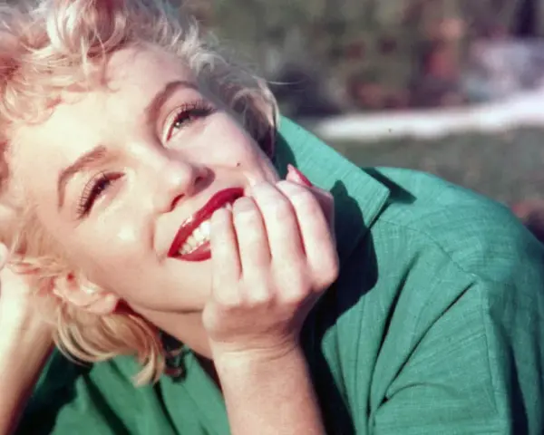 Marilyn Monroe, ikona kina, w zielonej sukience, z dłonią przy ustach, uśmiecha się promiennie.