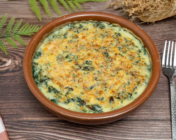Delicioso plato de espinacas a la crema gratinadas con queso, servido en cazuela de barro. Un bocado cremoso y reconfortante.