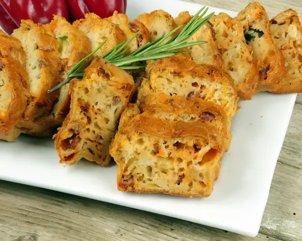 Tranches d'un cake salé au chorizo et poivron, garni de romarin, sur une assiette blanche.