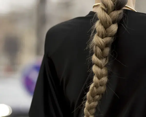 Gruby, blond warkocz opada na czarne ramię. To jedna z tych fryzur z warkoczem, które przyciągają wzrok.