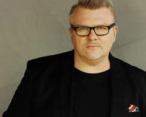Rafał Michalak w czarnym garniturze i okularach, z charakterystyczną bródką. W kieszeni marynarki ozdobna poszetka.