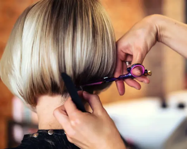 Fryzjerka modeluje cieniowany bob do ramion, używając nożyczek i grzebienia.