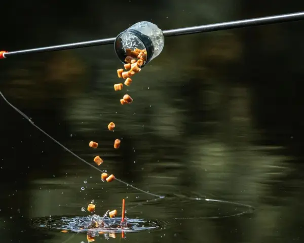 Karmnik method feeder wysypuje zanętę do wody, tworząc chmurę przynęty dla ryb.
