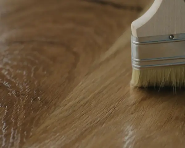 Brocha aplicando un acabado brillante sobre madera, mostrando diferentes tipos de barniz para madera.