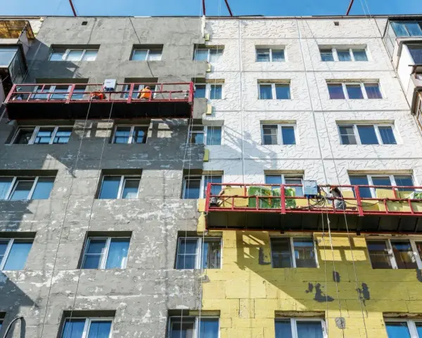 Remont bloku mieszkalnego w toku. Czy remont mieszkania trzeba zgłaszać? Pracownicy na rusztowaniach ocieplają budynek.