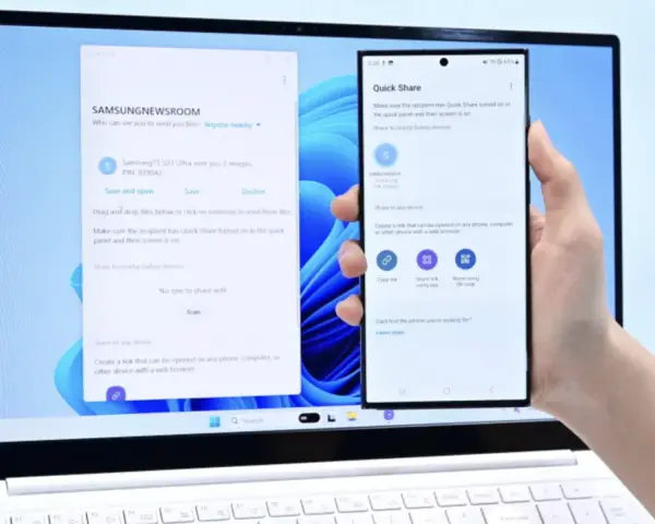 En hand håller en Samsung-telefon framför en laptop. Laptopen visar ett fönster för filöverföring, vilket underlättar att byta från iPhone till Samsung.
