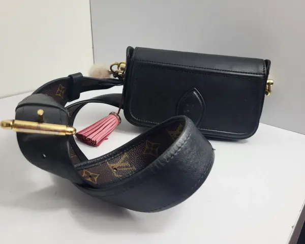 Elegancka, czarna louis vuitton torebka z ozdobnym, różowym pomponem i paskiem z monogramem.