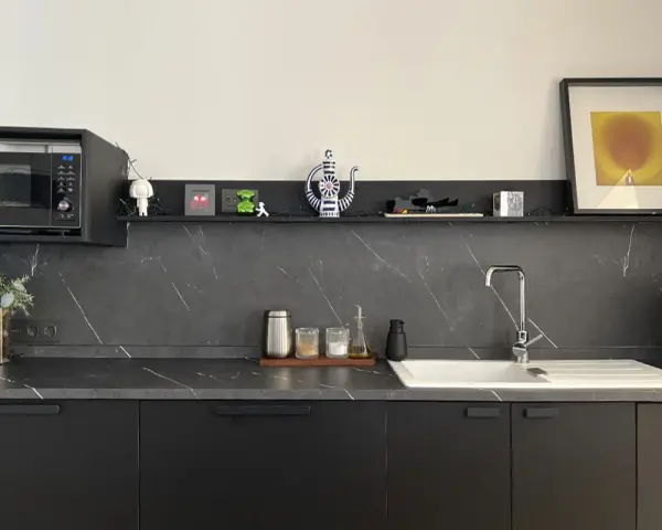 Encimera de cocina negra con vetas blancas, lista para cambiar. Microondas, fregadero y decoración moderna.