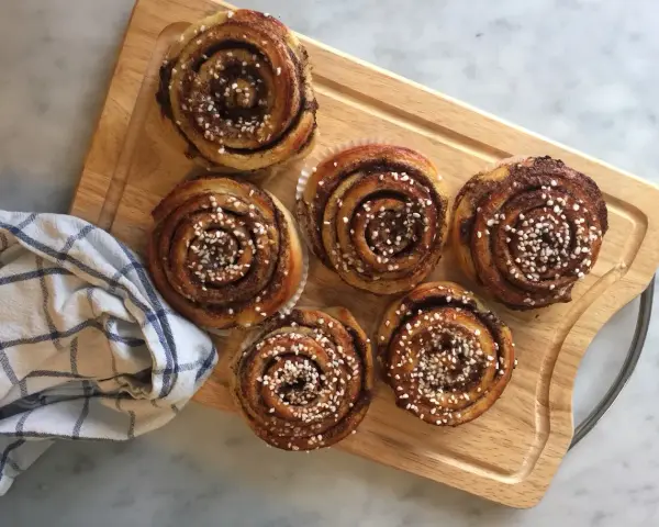 Sju gyllene kanelbullar med pärlsocker, redo att avnjutas. En härlig påminnelse om hur bakar man.