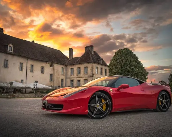 Czerwone Ferrari zaparkowane przed zabytkowym budynkiem podczas zachodu słońca.