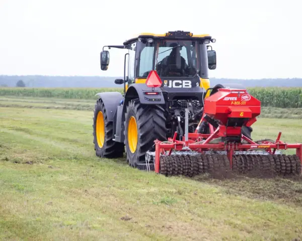 Ciągnik JCB z rozsiewaczem nawozu na polu.