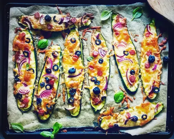 Zucchini-Hälften mit Käse, Oliven, Zwiebeln und Salami, die wie Pizza belegt sind. Sie schmeckt zucchini auf pizza!