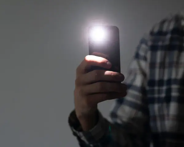 Dłoń trzyma smartfon z włączoną latarką.